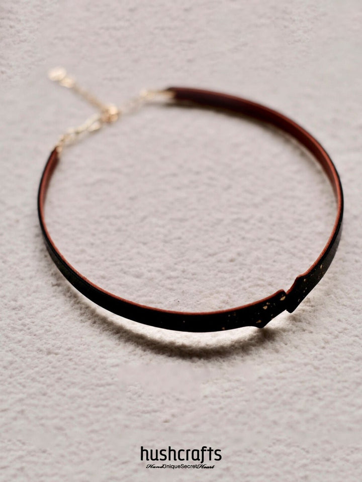 Close-up of HushCrafts black goatskin leather choker, featuring shimmering gold leaf and a bell pendant – a stylish and minimal day collar.