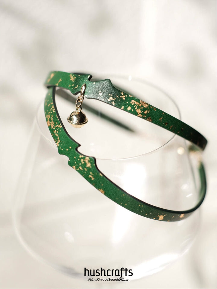 Green leather choker day collar by HushCrafts – lightweight and refined, with gold leaf pattern and a dangling bell charm.