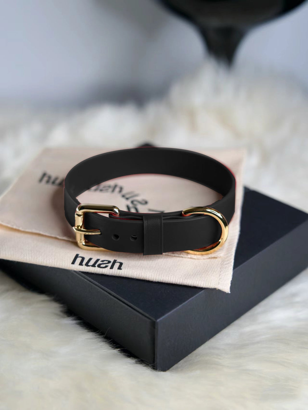 Elegant black leather collar with gold hardware, featuring a sturdy buckle and D-ring, displayed on a branded Hush pouch for a luxurious touch.