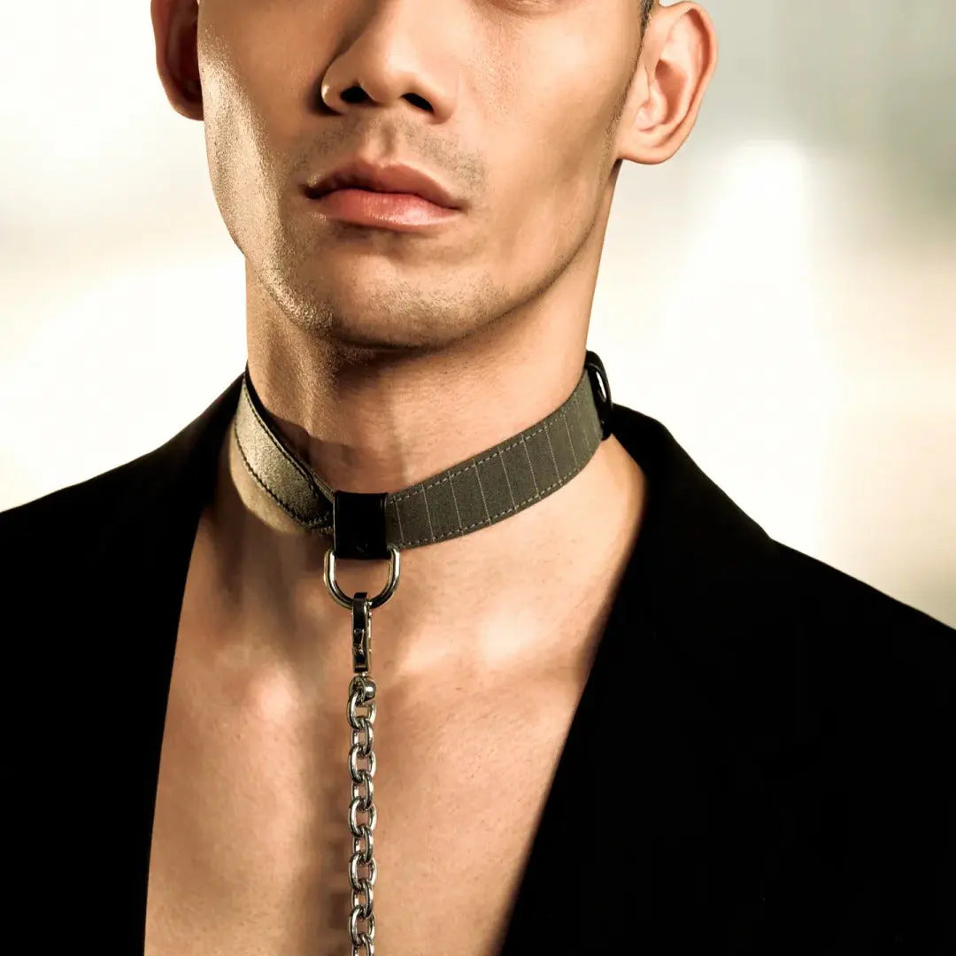 A close-up portrait of a man wearing a dark collar with a hanging chain, styled with a black open-collar shirt. The image has a white bottom border with the brand logo 'BOUND | 无隙'.