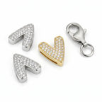 Three silver pendants shaped like arrows and a heart, with a gold heart pendant and a silver clasp on a white background.
