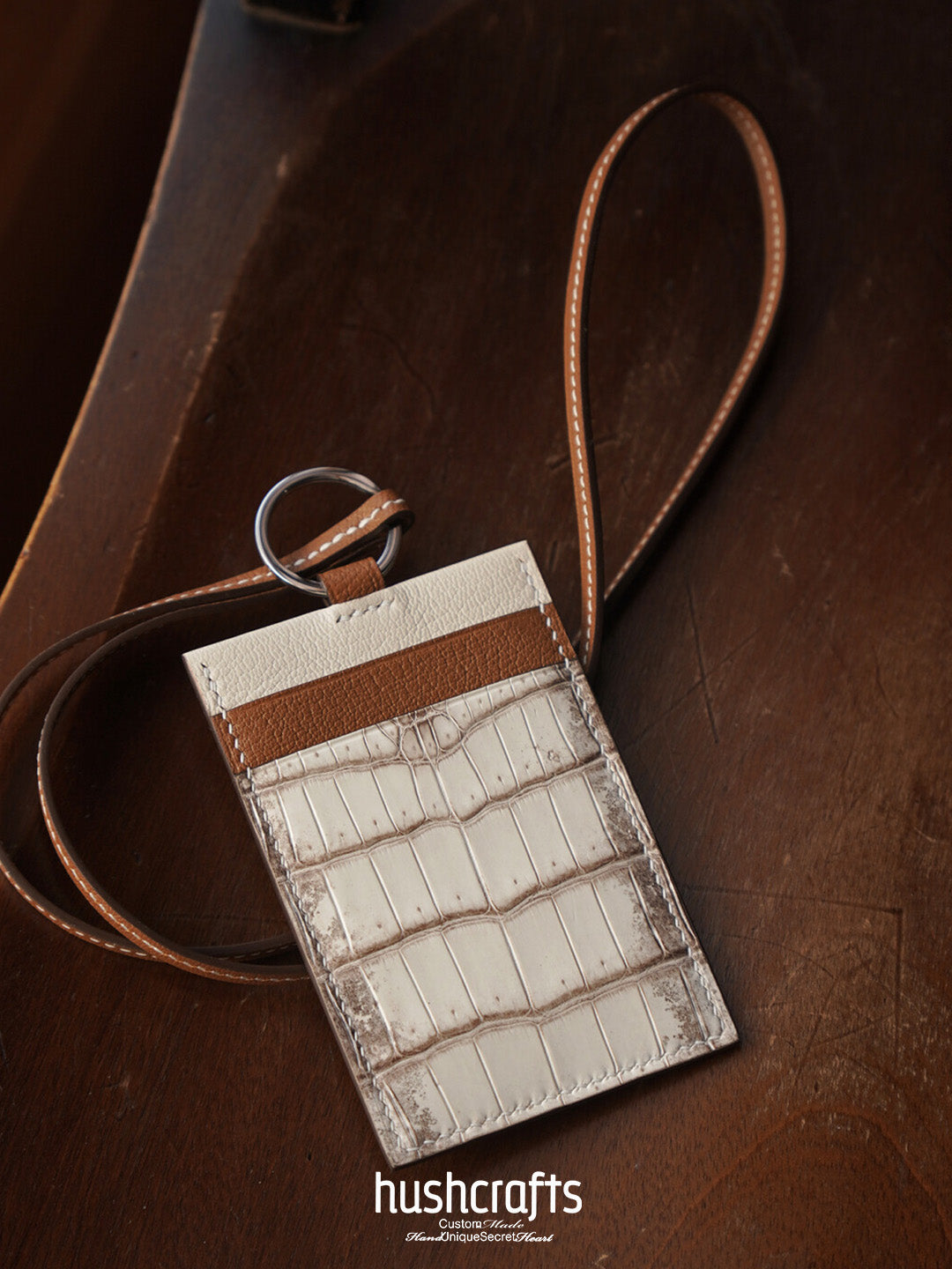 Leather cardholder with strap on a wooden surface, featuring the brand 'hushcrafts'.