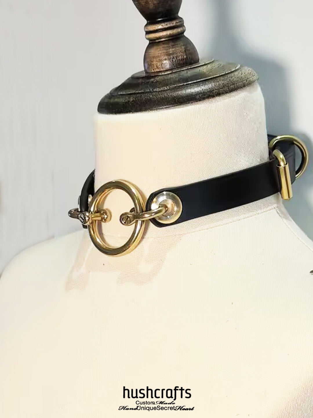 Black leather choker with gold rings on a mannequin bust, branded 'hushcrafts'.