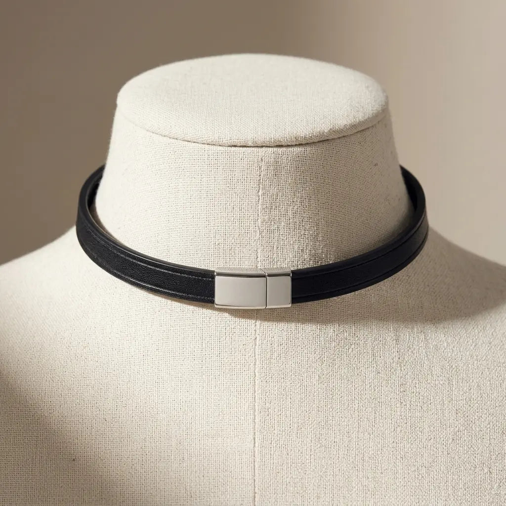 A black leather choker collar with a polished silver rectangular clasp, displayed on a cream-colored fabric jewelry mannequin bust.