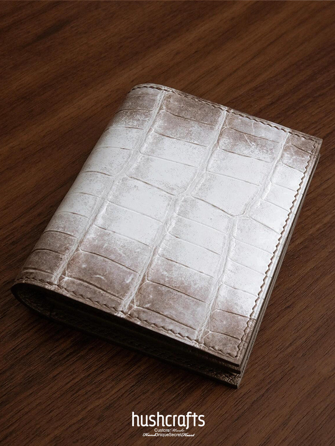 Leather wallet with crocodile pattern on a wooden surface, featuring the brand 'hushcrafts'.