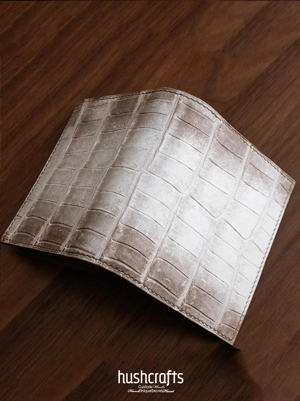Brown leather wallet with crocodile pattern on a wooden surface, featuring the brand 'hushcrafts'.