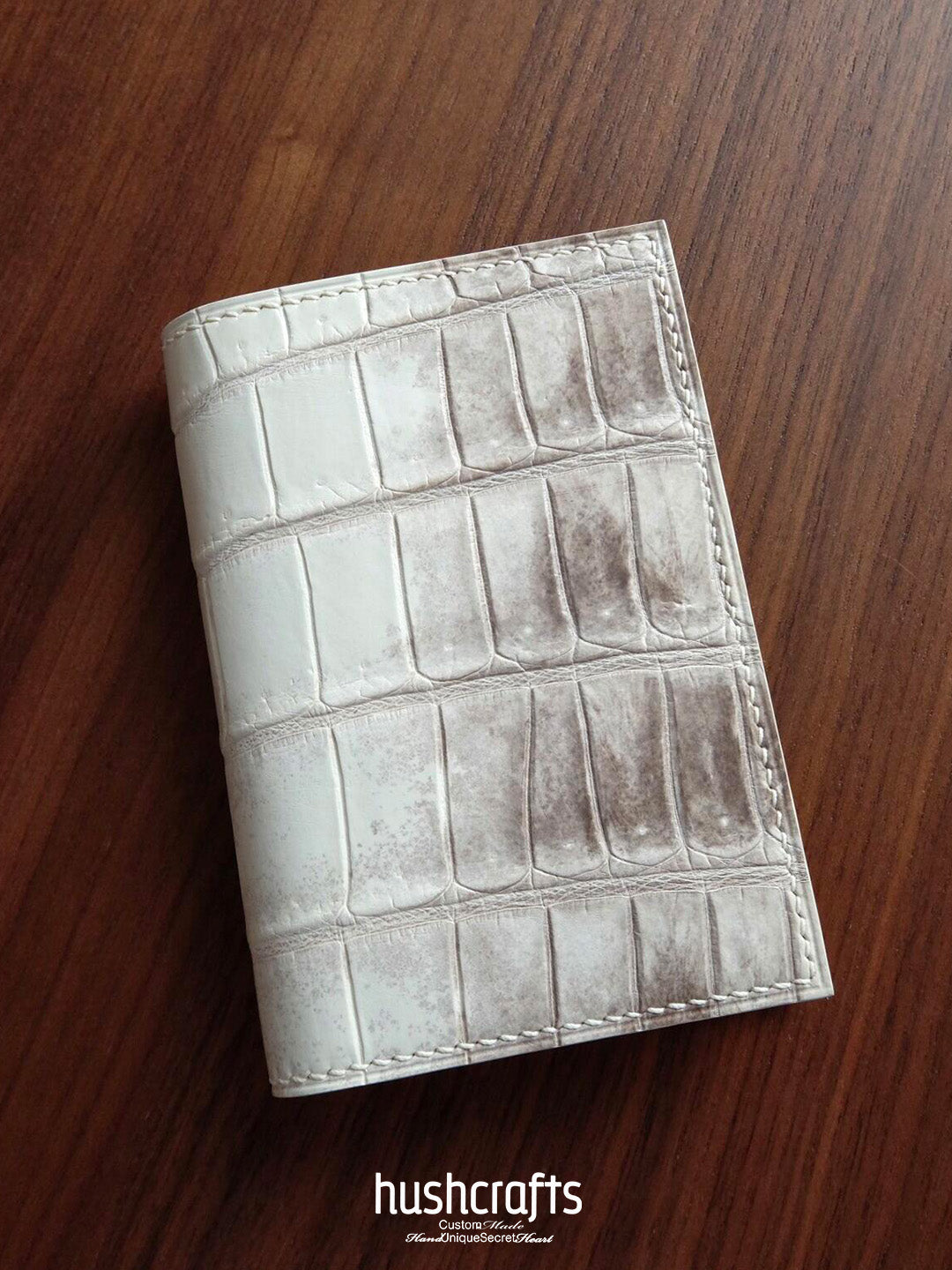 White textured wallet on a wooden surface with 'hushcrafts' branding.