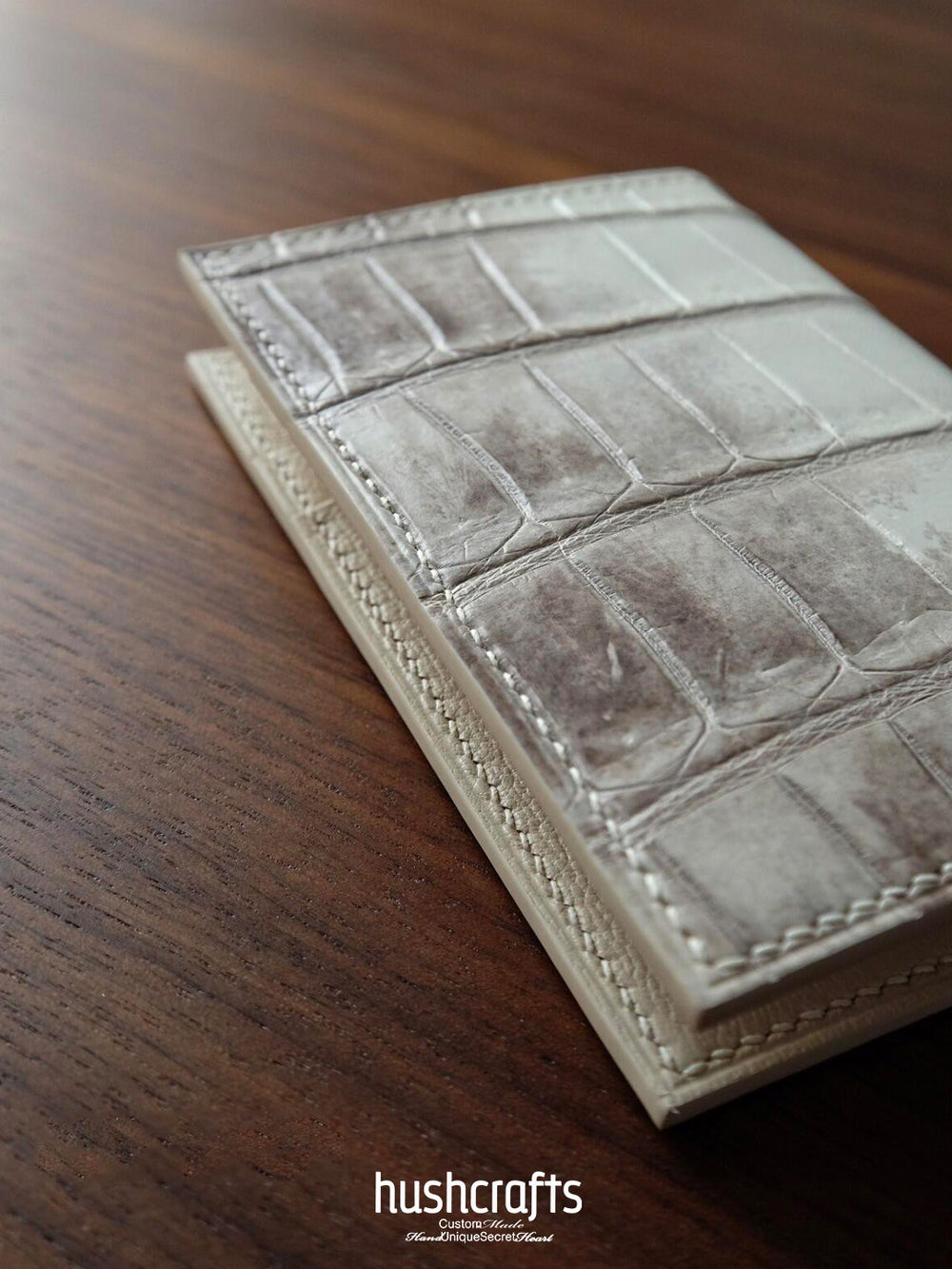 Leather wallet with crocodile pattern on a wooden surface, featuring the brand 'hushcrafts'.