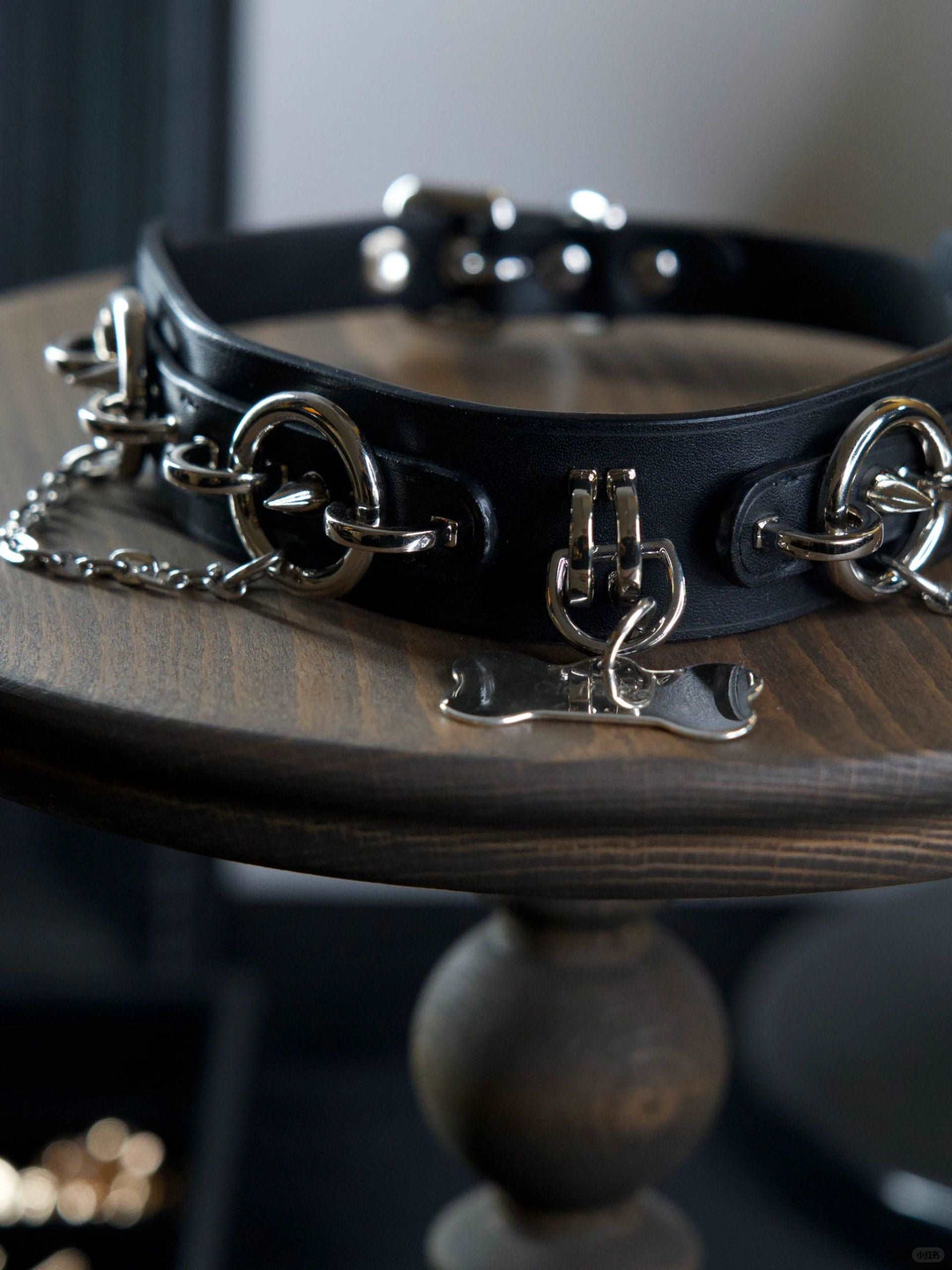 A black leather BDSM collar with locks on chains and choker collars, featuring a triskelion necklace detail, crafted by HushCrafts.