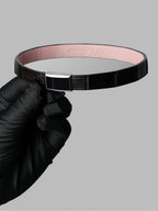 Black crocodile leather choker with pink lambskin lining and a stainless steel magnetic clasp, held in a black-gloved hand.