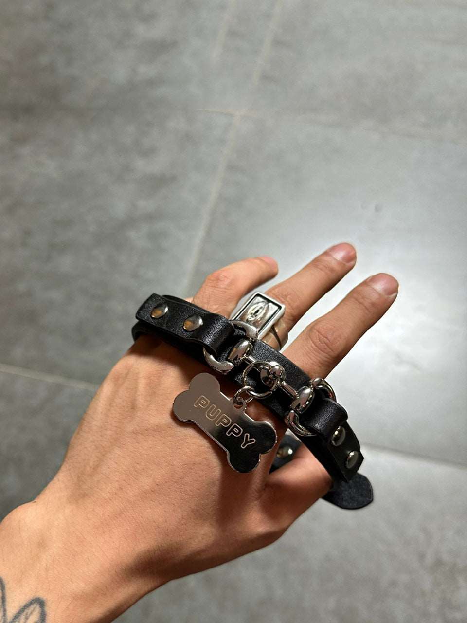 A black leather submissive day collar featuring a lock and key necklace design with a clasp chain, symbolizing the meaning of being collared in a relationship.